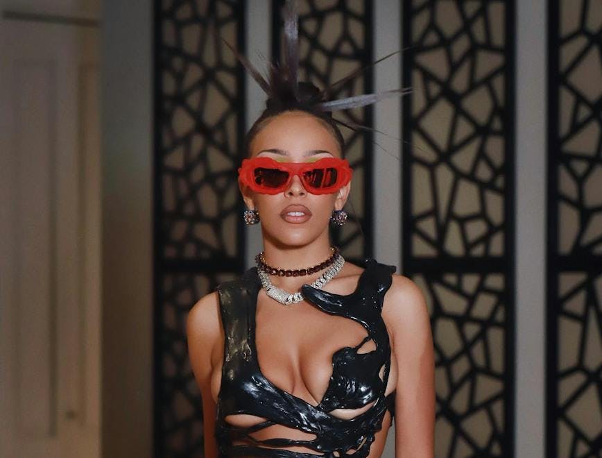 Doja Cat wearing a black leather crop top and black pants with red sunglasses. 