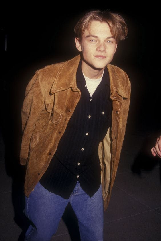 young leonardo dicaprio in a brown jacket, black button up, and jeans