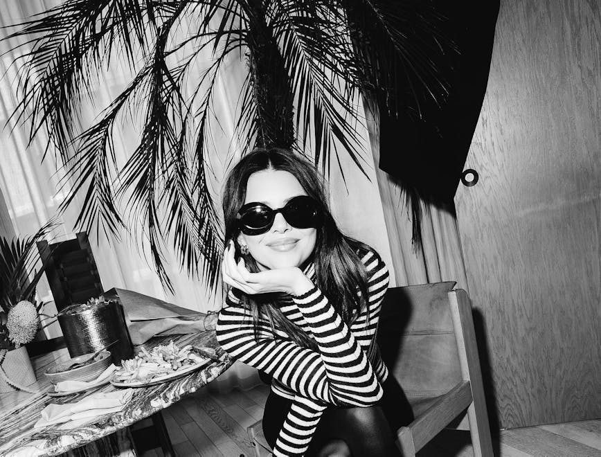 Black and white photo of a woman in a striped shirt sitting down wearing sunglasses.