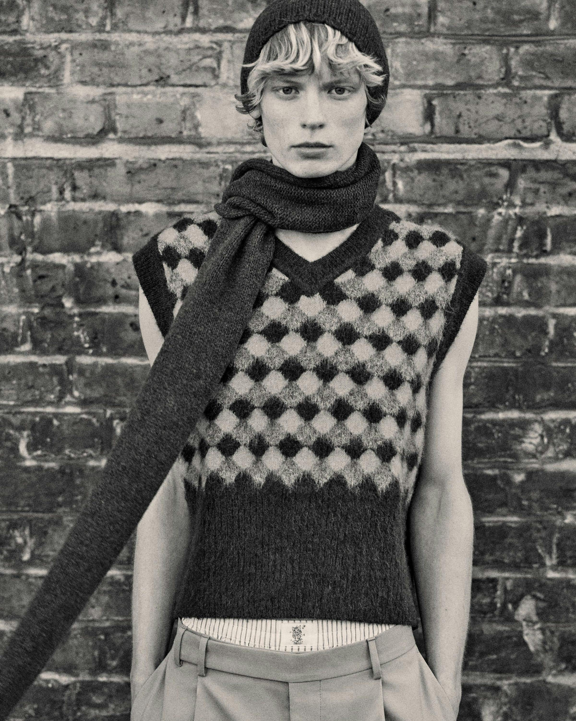 a model in a sweater vest, beanie, and chunky scarf for harry lambert x zara collaboration