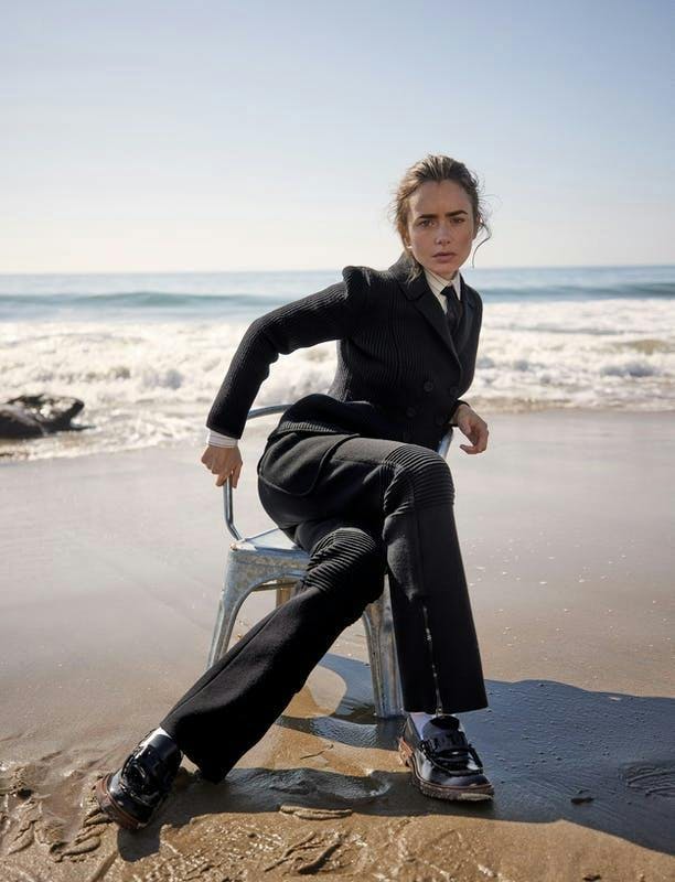 Lily Collins in a suit in a chair on the beach