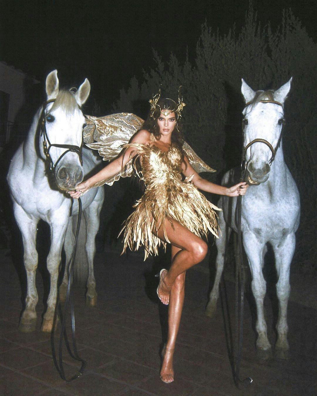 kendall jenner in a gold fringe mini dress posing next to two white horses
