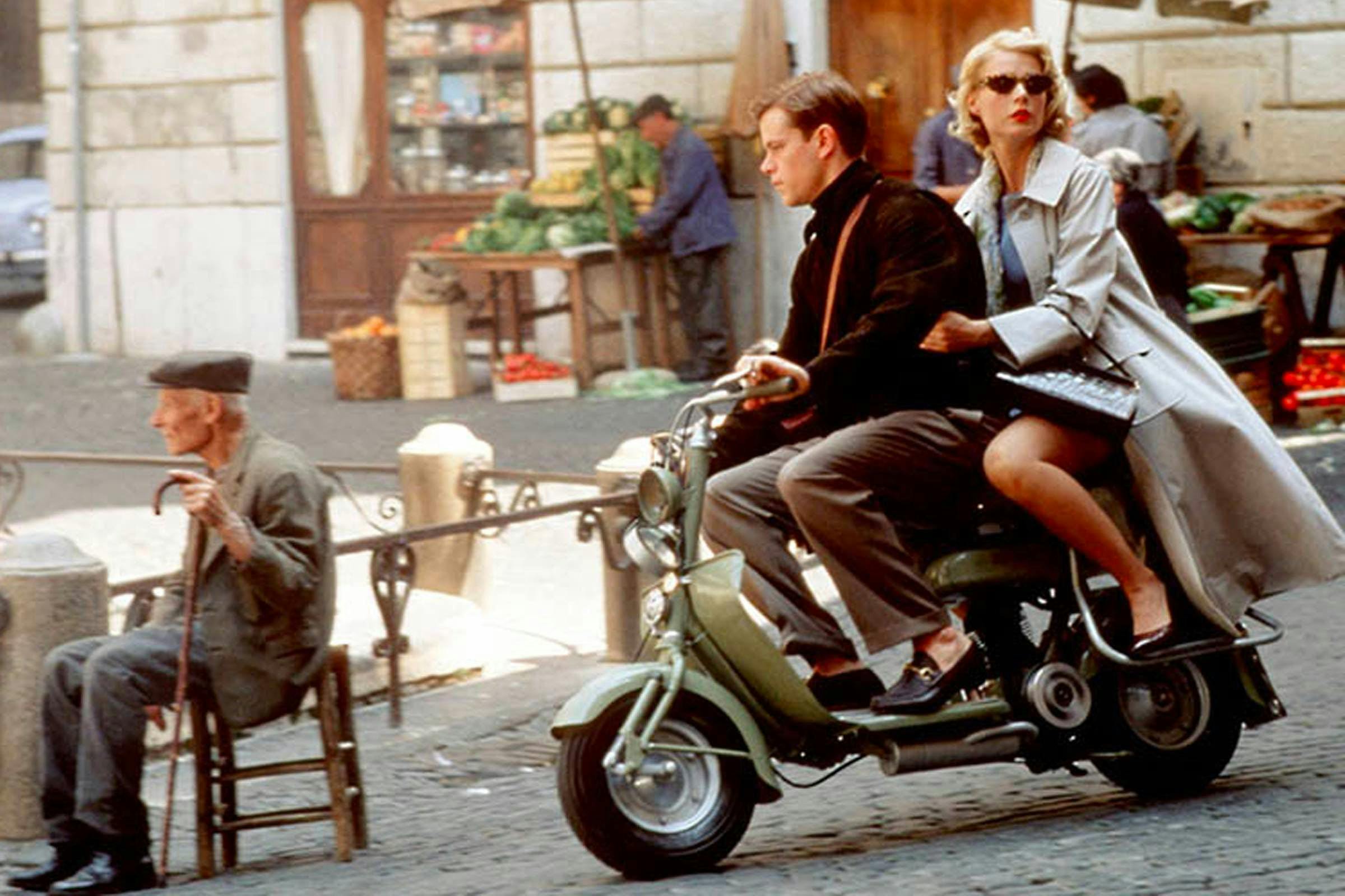 A woman and man riding a motor scooter on the streets of Italy.