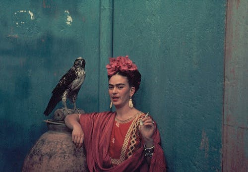 Frida Kahlo in a red top and headscarf next to a bird.