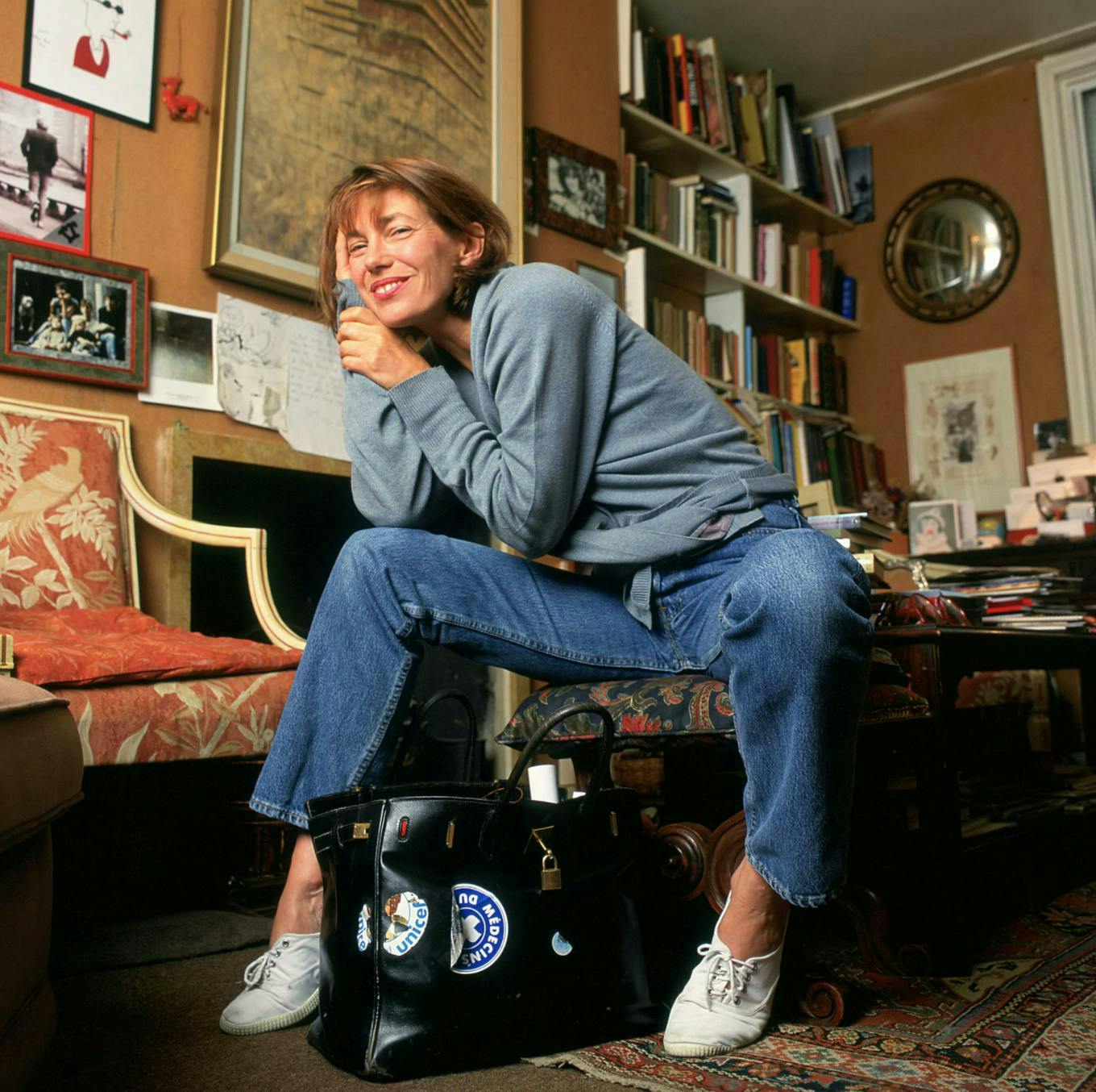 jane birkin sitting on a chair beside the hermes bag named after her