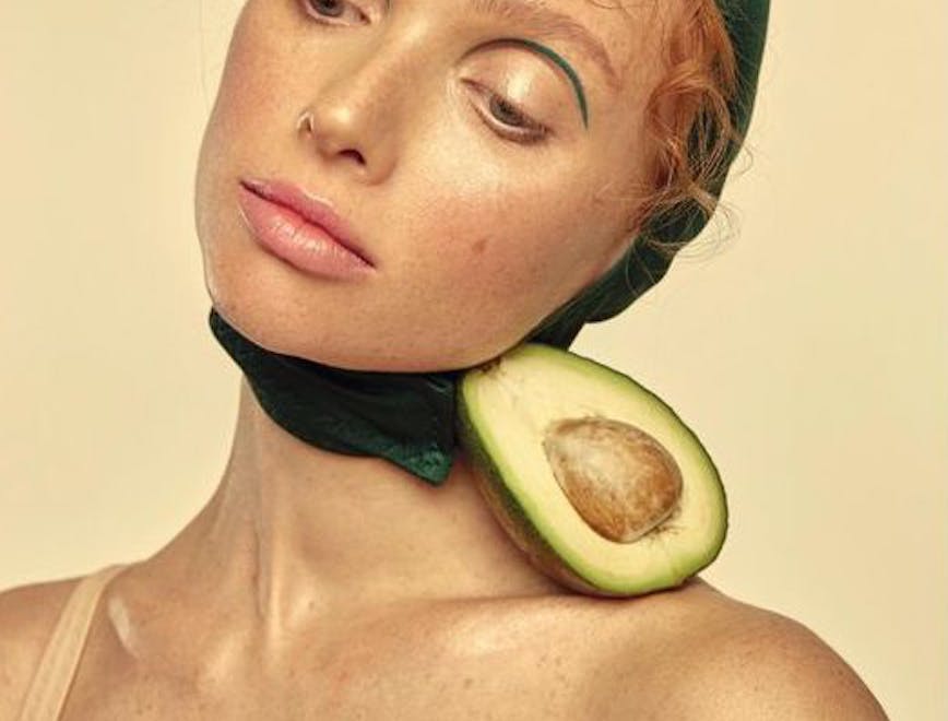 Woman wearing avocado inspired earrings against yellow background.