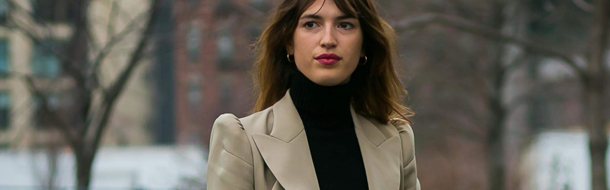 Jeanne Damas in a light brown blazer, black top, and blue jeans French girl style icons.