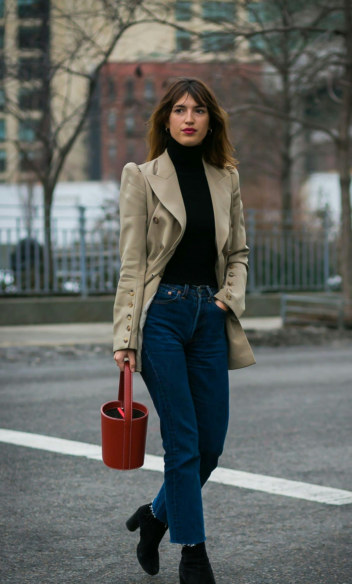 Jeanne Damas in a light brown blazer, black top, and blue jeans French girl style icons.