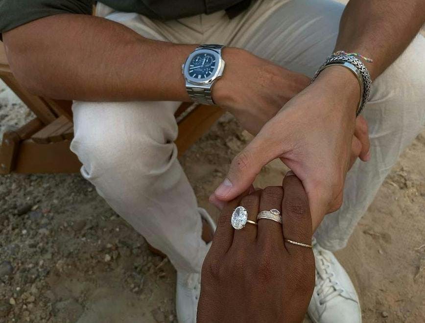 Oval diamond ring on a black female hand, held by a tan male hand. 