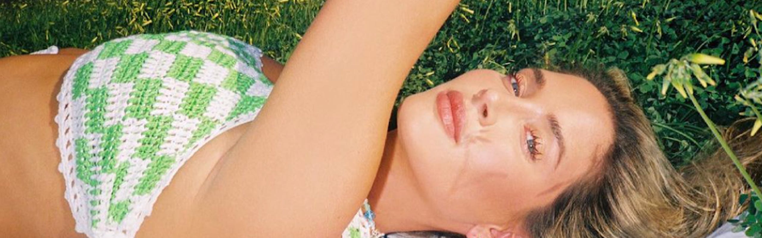 Woman laying down on a blanket on grass, wearing a green and white checkered crochet bra