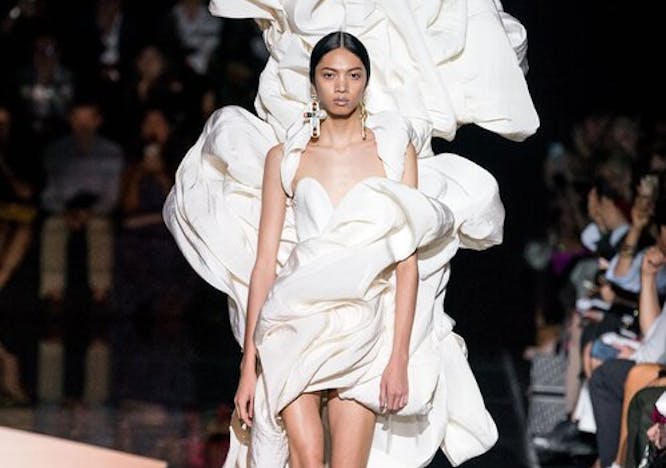 Model walks down black runway in dramatic, poofy, white Schiaparelli wedding dress.