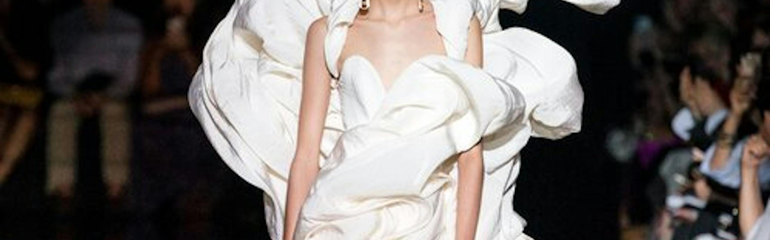 Model walks down black runway in dramatic, poofy, white Schiaparelli wedding dress.