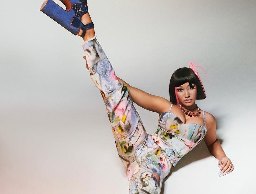 Nicki Minaj in a colorful Marc Jacobs jumpsuit and blue block heels shoes against a white backdrop.