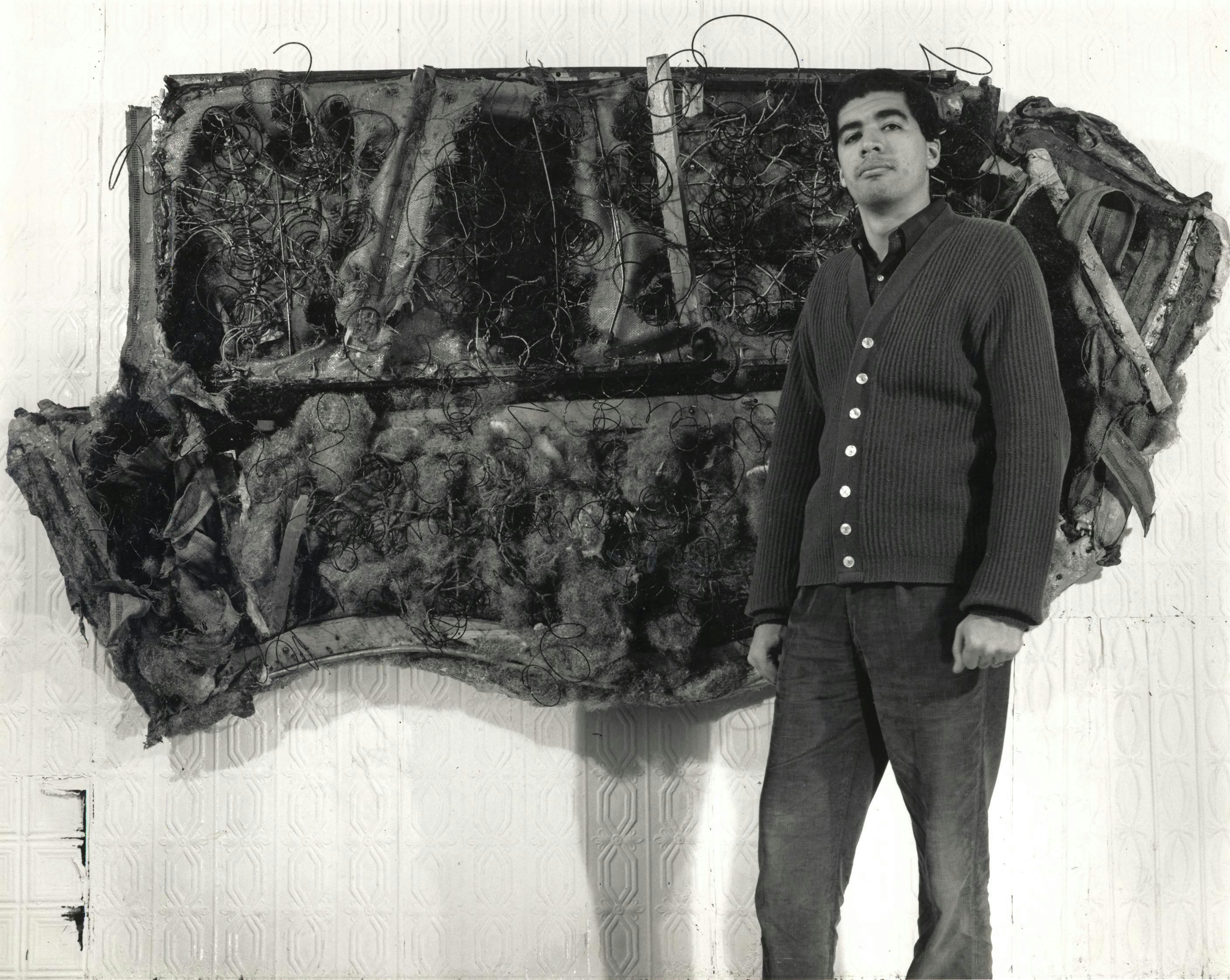 Work by Raphael Montañez Ortiz rendered in black and white. Ortiz pictured in front of their work.