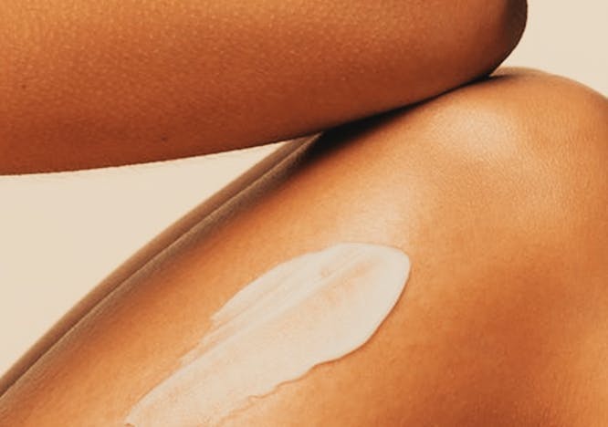 Closeup image of a woman's elbow touching her knee with a line of white moisturizer or sunscreen on her thigh. 