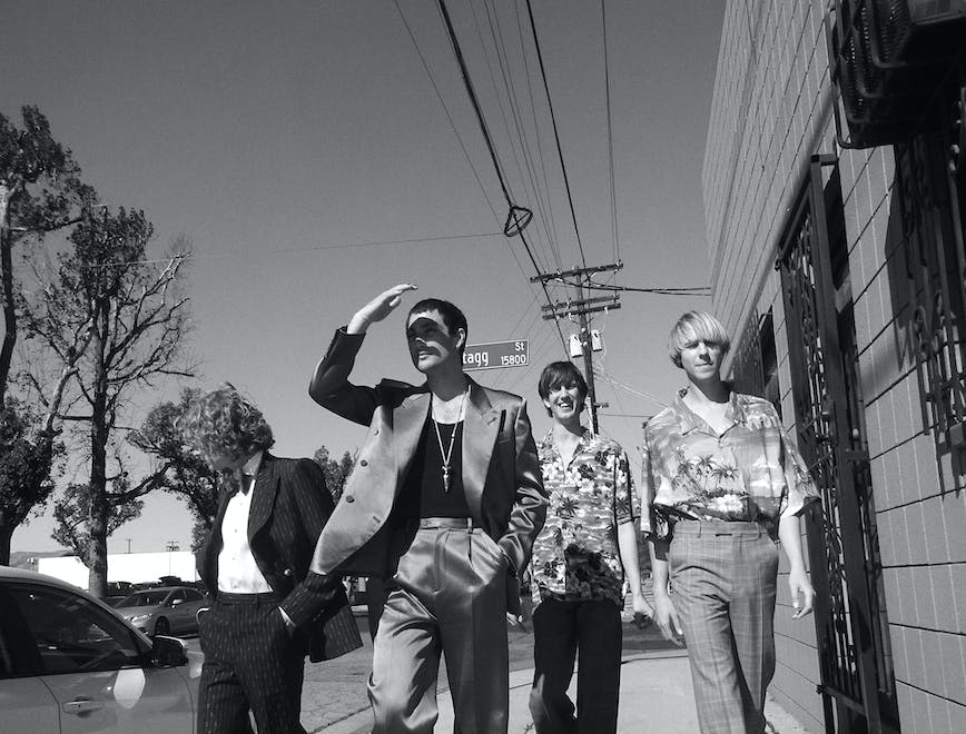 In a black and white photo, Australian band Parcels walk on the street beside a tree with a power line above them. 