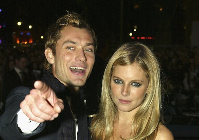Jude Law and Sienna Miller pose for the camera both wearing all black. Law wears a black scarf and Miller carries a beaded bag.