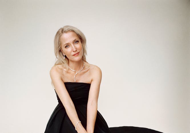 Gillian anderson sitting down in a black dress and heels