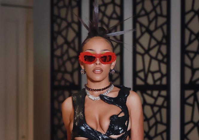 Doja Cat wearing a black leather crop top and black pants with red sunglasses. 
