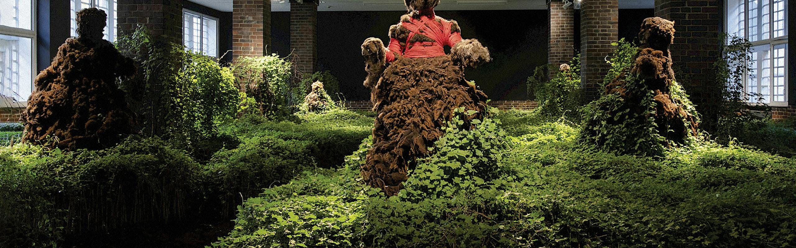 A collection of green, brown, and pink moss like flowers cover statues shaped like women to make "Open cirlce Lived Relation;