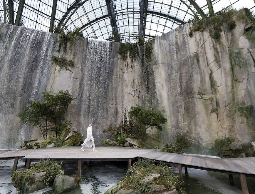 A model walks in a white dress in front of the rock waterfall located in the Grand Palais in Paris.
