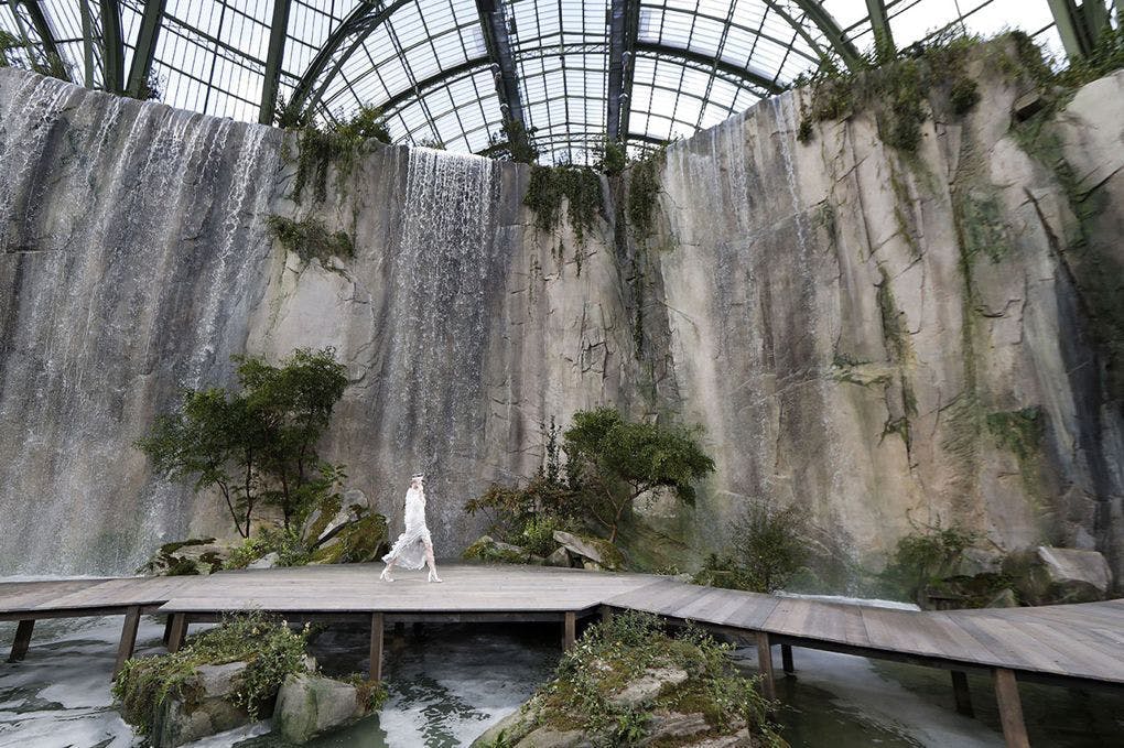 A model walks in a white dress in front of the rock waterfall located in the Grand Palais in Paris.