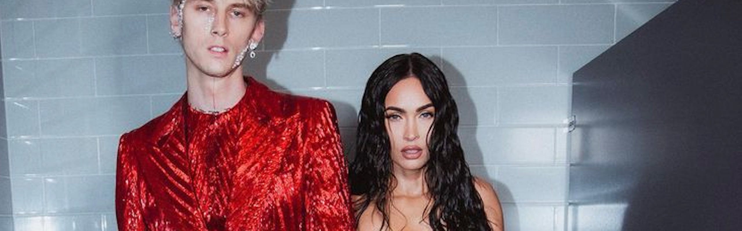 Megan Fox wears a sheer form fitting dress while standing next to fiancé Machine Gun Kelly, who wears a red sparkly suit.