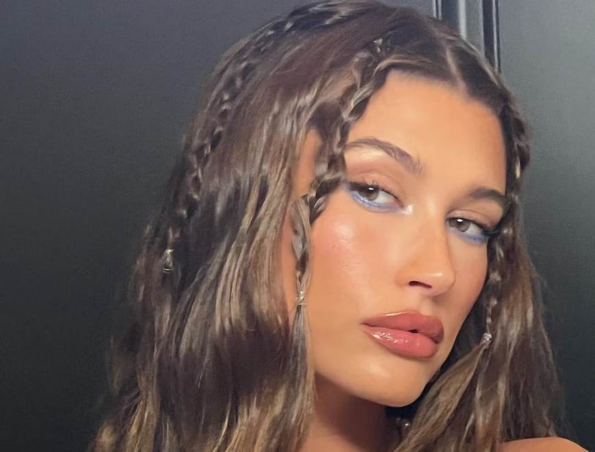Hailey Bieber posing for the camera with braids in her hair and colorful makeup