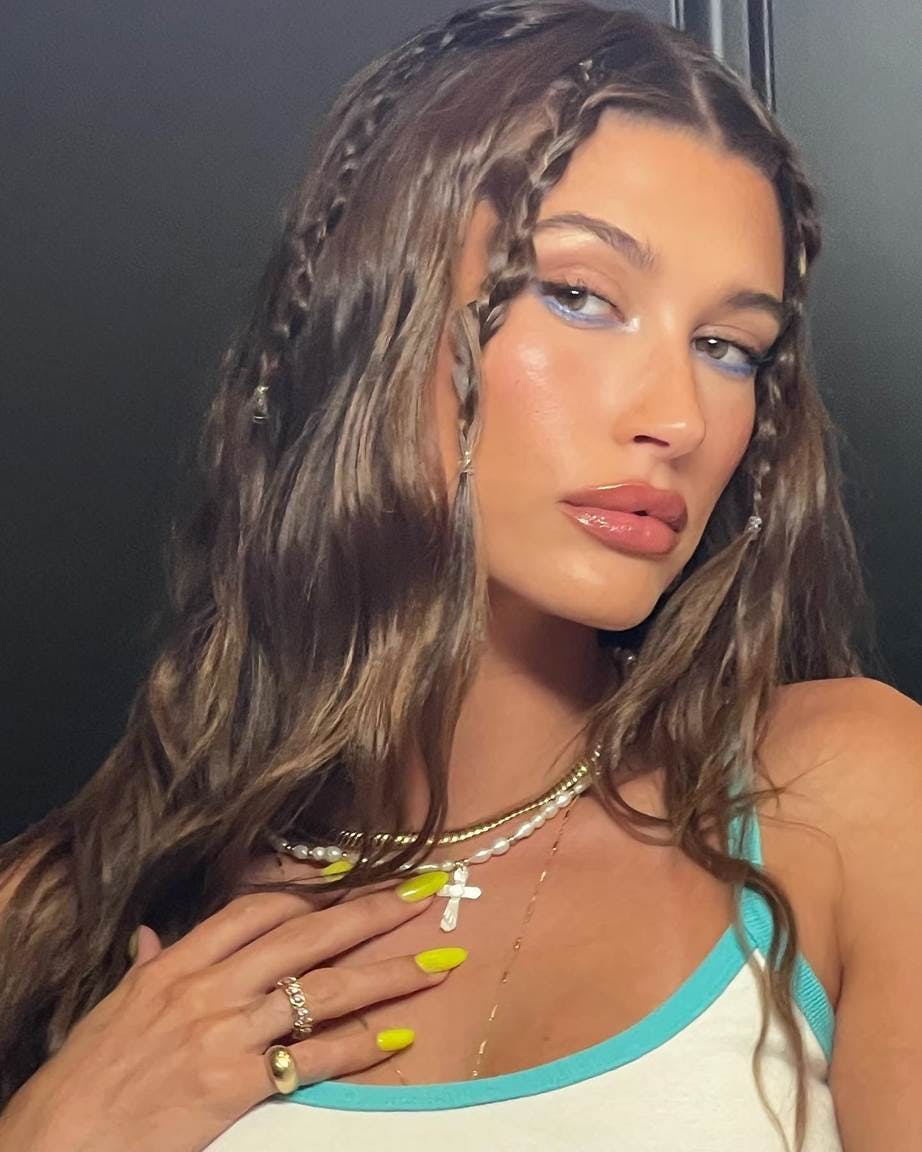 Hailey Bieber posing for the camera with braids in her hair and colorful makeup