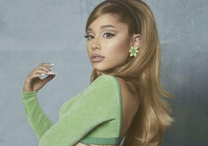 Ariana Grande wears green crop top with matching green flower earrings as she poses in front of a grey back drop.