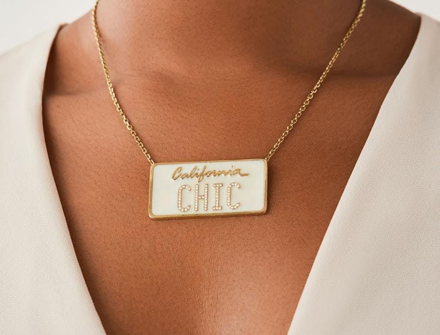 A square white necklace, mimicking a license plate, with the word "California" in cursive and the word "chic" in capital letters. 