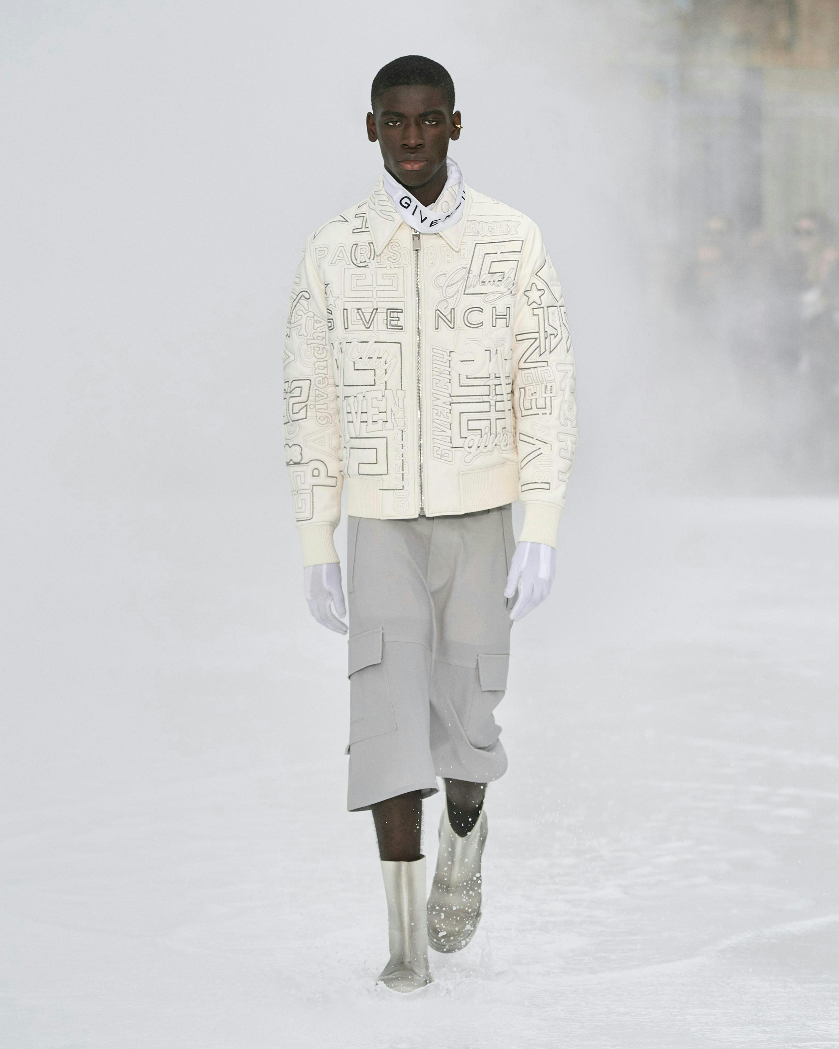 Model for Givenchy wearing a cream jacket and grey cargos.