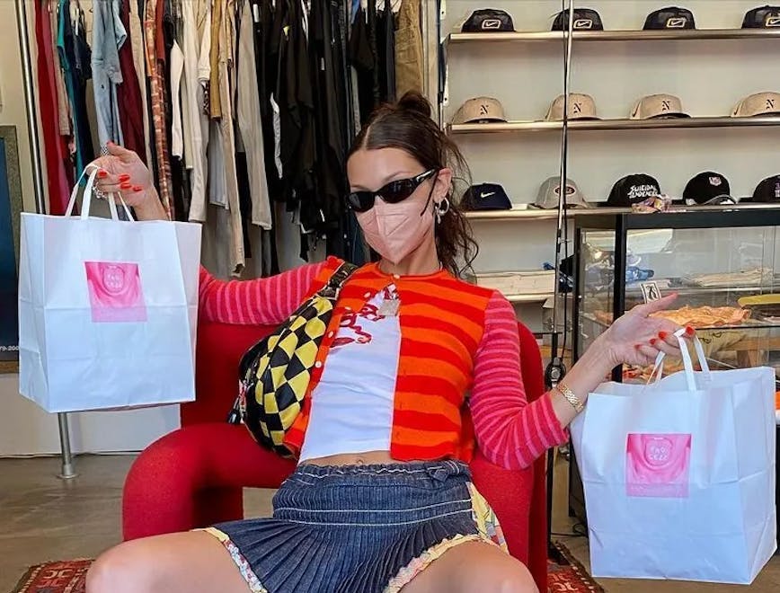 Bella Hadid holding two shopping bags sitting in a chair