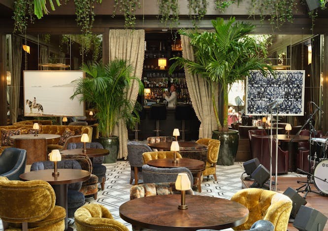 The Ned NoMad hotel is pictured. Tables with yellow chairs and lots of greenery. 