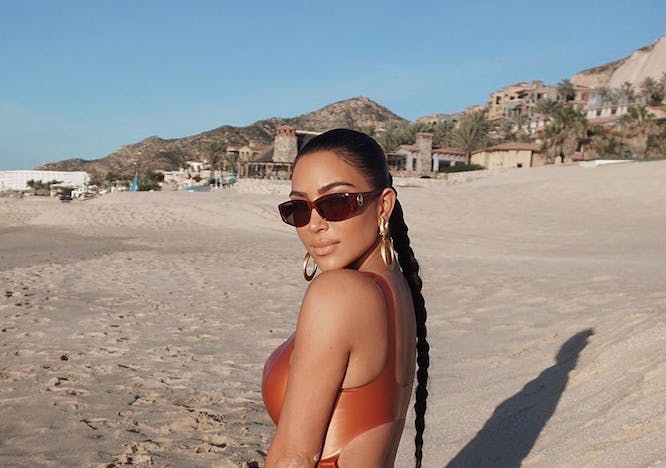 Kim Kardashian in a bronze monokini, posing in the sand. 