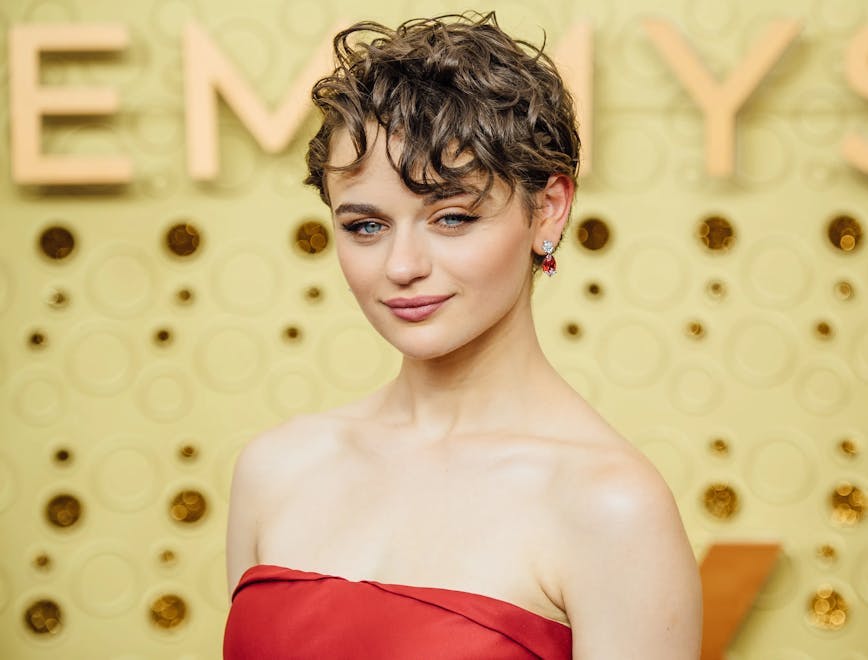 Joey King poses in a red dress behind an Emmy's backdrop. 