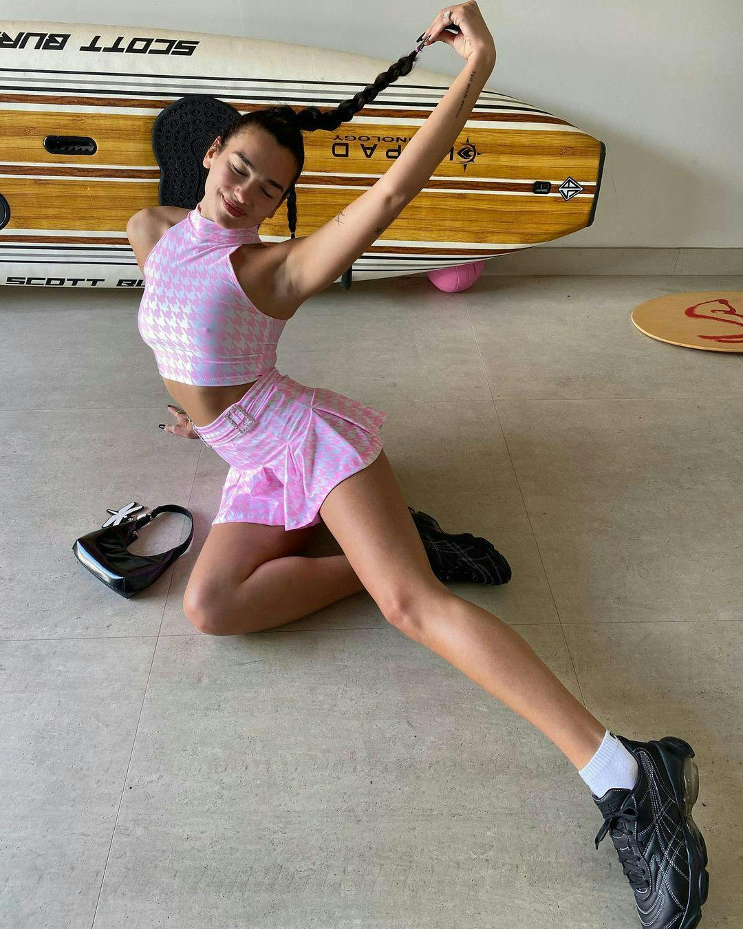 Dua Lipa poses in a matching hot pink houndstooth skirt and crop top, a preppy summer trend.