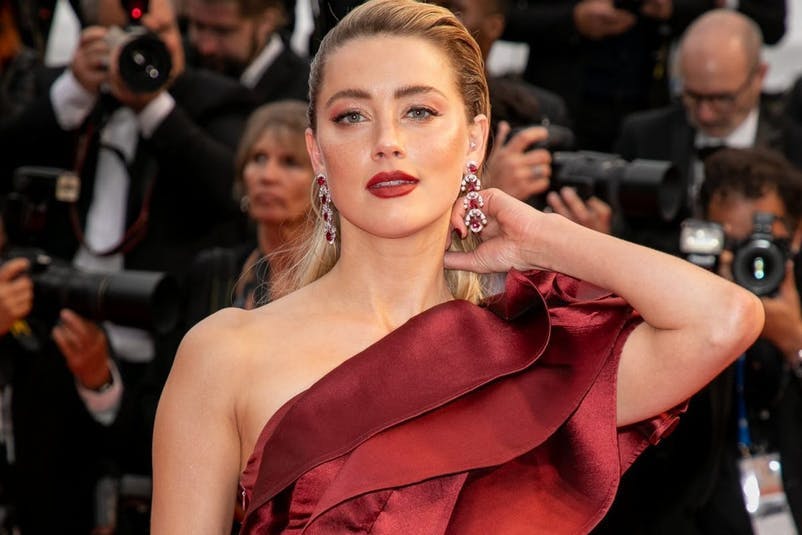 Amber Heard on the red carpet with slicked back hair and red lipstick.