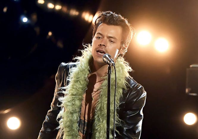 Harry Styles in a black leather jacket and green feather scarf.