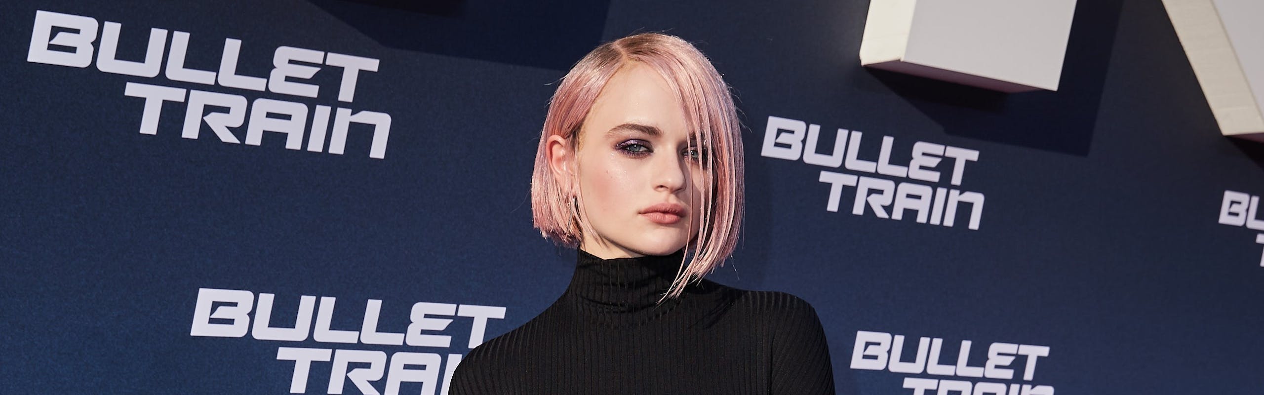 Joey King on a red carpet for Bullet Train wearing a black jumpsuit by Balenciaga and a pink bob haircut.