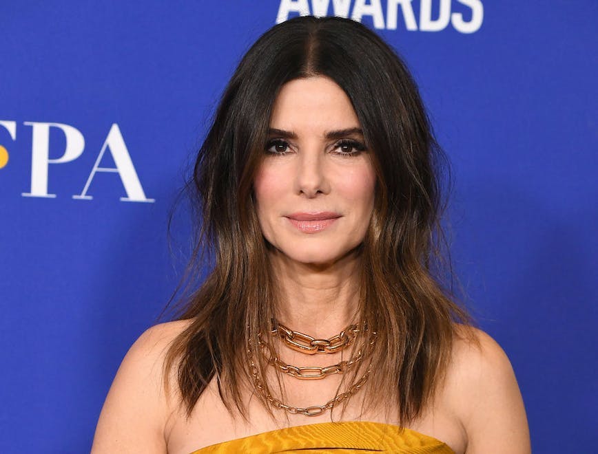 Sandra Bullock poses on a red carpet in a yellow strapless dress.