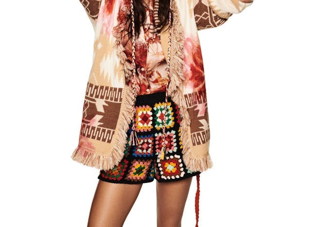 Model wearing crochet shorts and hat, a tie dye shirt and a printed cardigan.