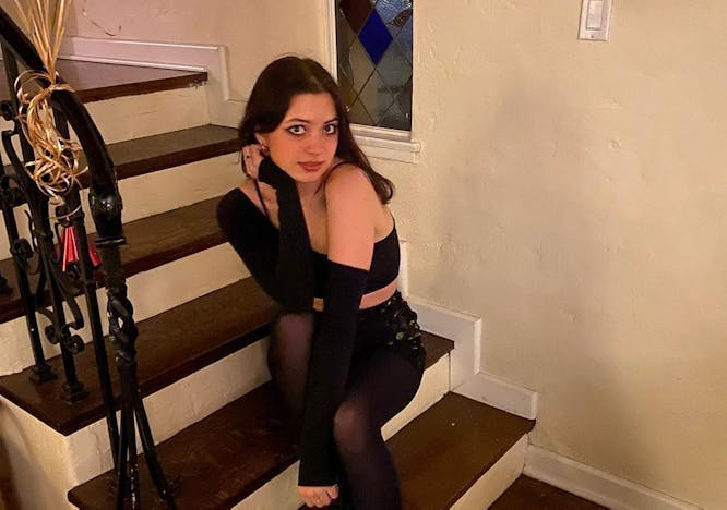 Lizzy McAlpie sits on a staircase and poses for a photo in an all-black outfit.