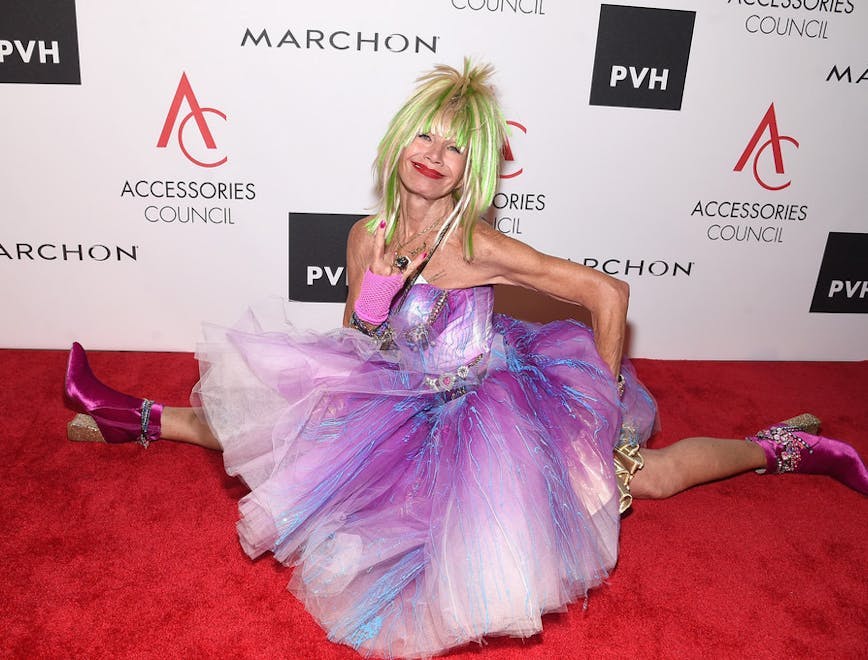 Betsey Johnson doing a split on a red carpet in a puffy purple dress