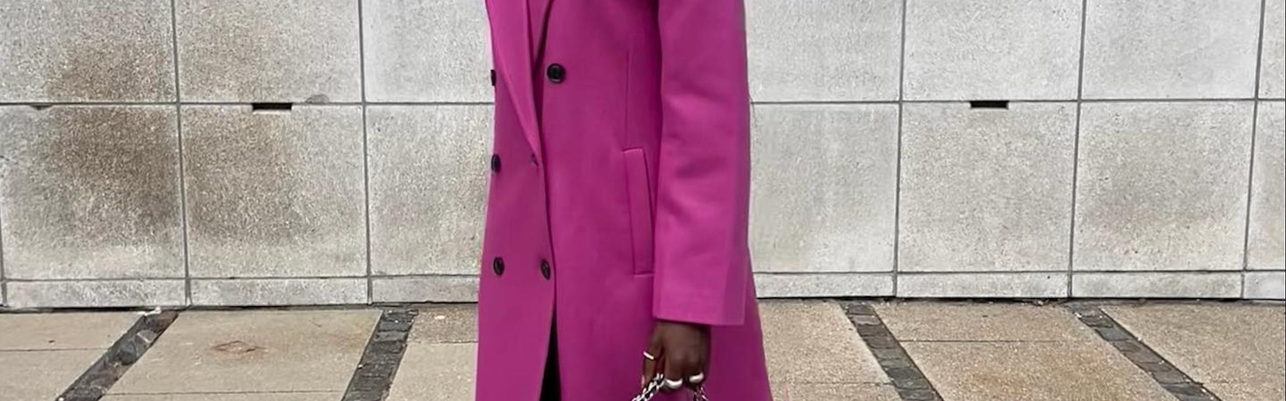 Woman wearing a long hot pink coat, a quilted Chanel bag and chunky sneakers