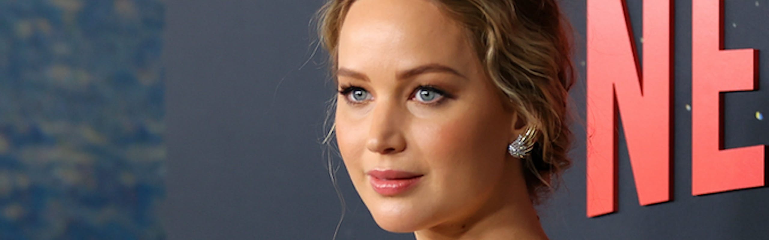 Pregnant Jennifer Lawrence poses for a photograph in a gold gown.