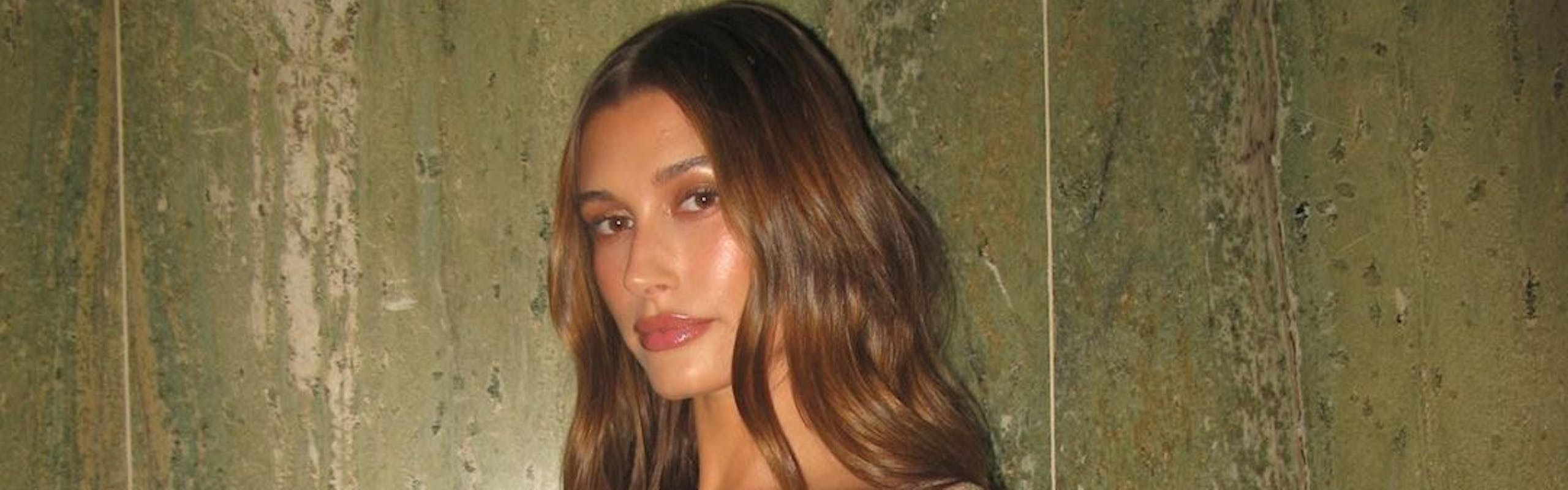Hailey Bieber poses against a green wall in a nude sequined dress.