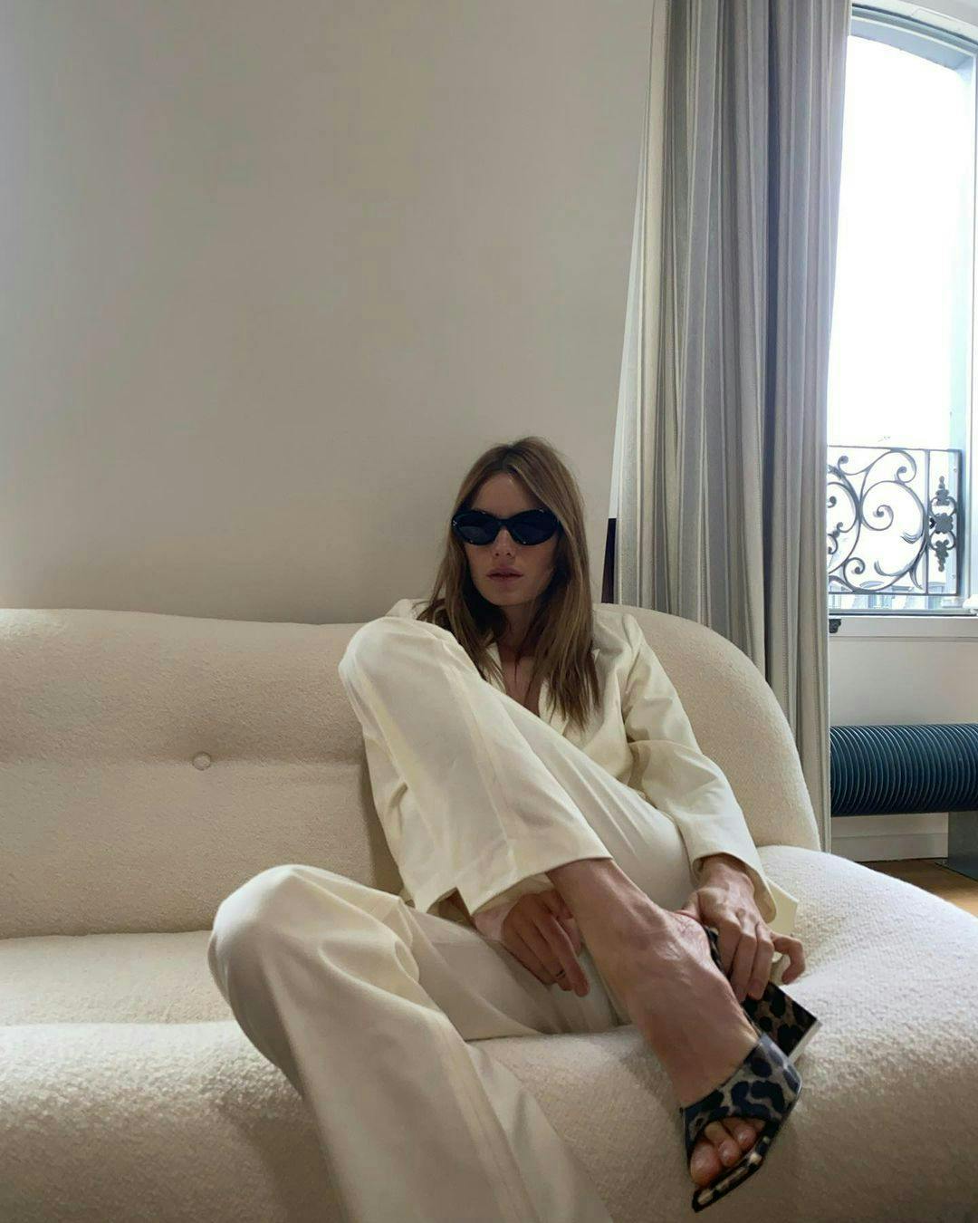 Camille Rowe in an all-white outfit and black shoes and sunglasses.