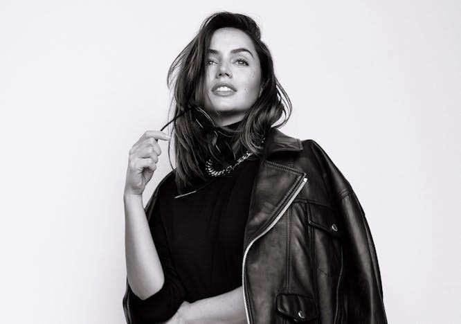 Black and white photo of Ana de Armas wearing a black turtleneck, leather jacket and leather and pants and chain necklace.