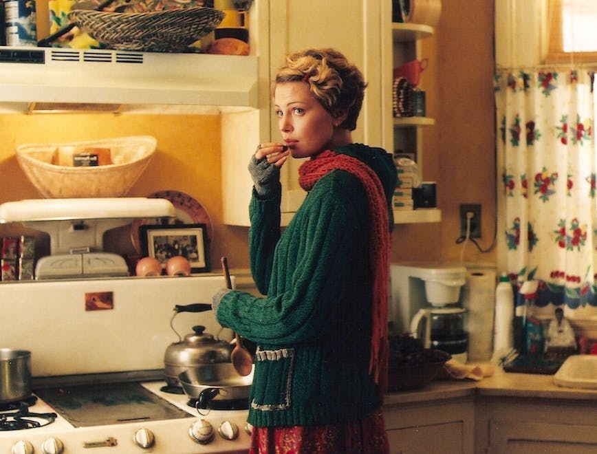 a woman in a green sweater and red scarf cooking in the kitchen